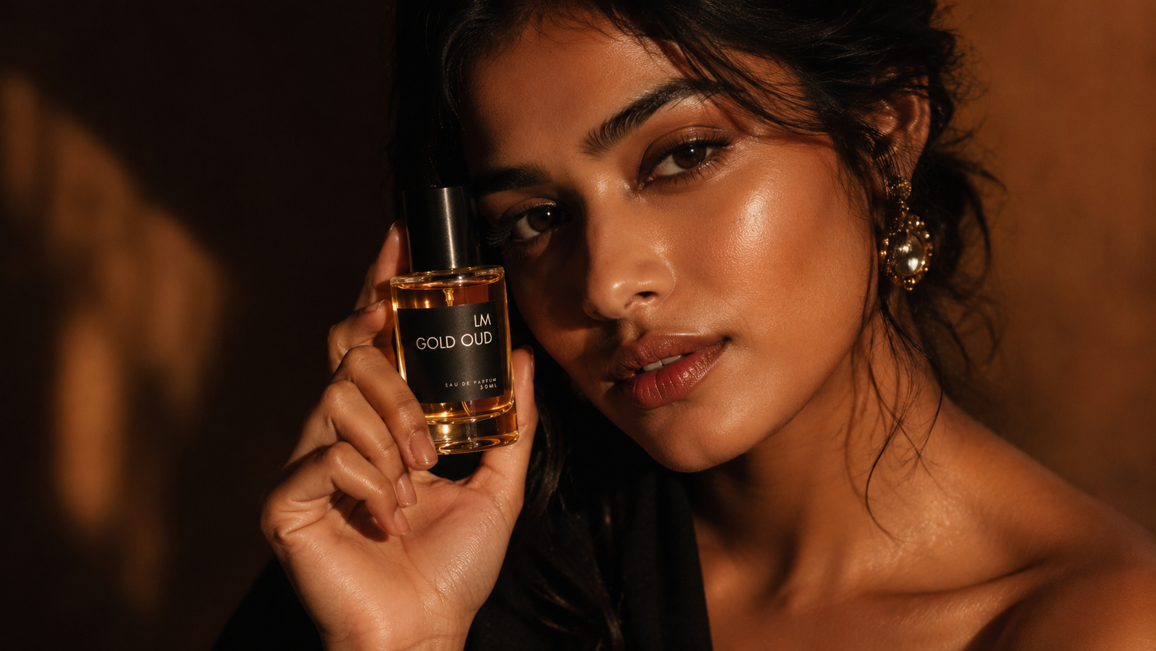 Woman holding a perfume bottle labeled 'GOLD OUD' against a warm-toned background